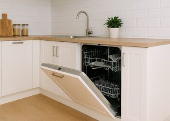 Bright kitchen featuring an open built-in dishwasher under a wooden countertop, white cabinets, stainless