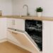 Bright kitchen featuring an open built-in dishwasher under a wooden countertop, white cabinets, stainless