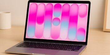 Laptop sitting open on a wooden desk displaying a colourful pink and blue screen