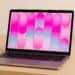 Laptop sitting open on a wooden desk displaying a colourful pink and blue screen