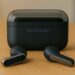 Samsung Galaxy Buds4 wireless earbuds resting on a wooden table with the charging case behind, photographed in a modern office setting
