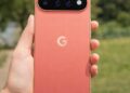 Coral Google Pixel 11 smartphone held outdoors showing rear camera bar and sleek design.