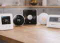Smart thermostats displayed on a light wooden kitchen countertop, showing different designs and screens, representing modern home heating technology.