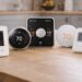 Smart thermostats displayed on a light wooden kitchen countertop, showing different designs and screens, representing modern home heating technology.