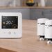 Smart heating devices from the Drayton Wiser system arranged on a kitchen table, including the main thermostat and two radiator valves, shown without any app interface.