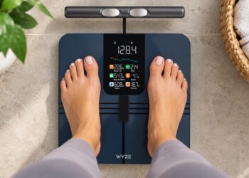 Person standing on a Wyze Scale BodyScan smart scale displaying body composition metrics, weight, BMI, muscle mass, body fat percentage, and wellness tracking data.