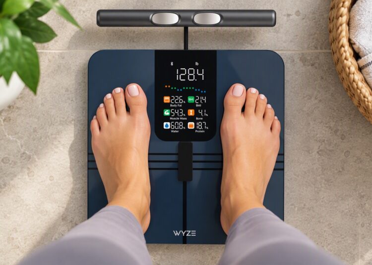 Person standing on a Wyze Scale BodyScan smart scale displaying body composition metrics, weight, BMI, muscle mass, body fat percentage, and wellness tracking data.