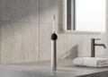 RANVOO AirJet X5 electric toothbrush standing on a modern concrete bathroom vanity countertop with a rolled towel and backlit mirror