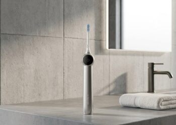 RANVOO AirJet X5 electric toothbrush standing on a modern concrete bathroom vanity countertop with a rolled towel and backlit mirror